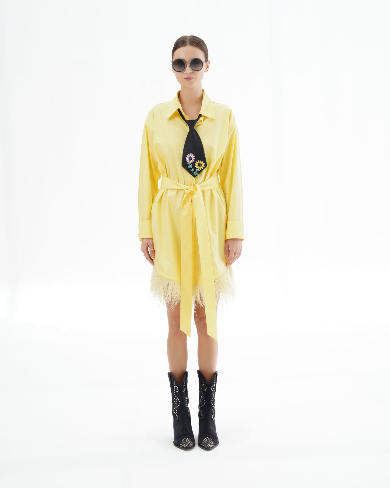 Woman wearing a yellow dress with a floral tie and black boots on a white background